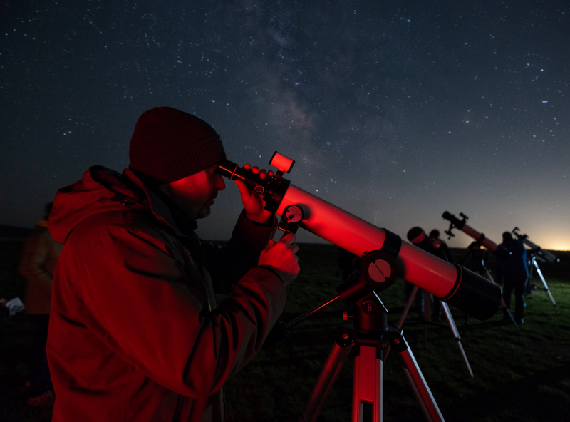 Astronomer looking through the eyepiece of a telescope at a star party under a dark sky with red headlamp light
