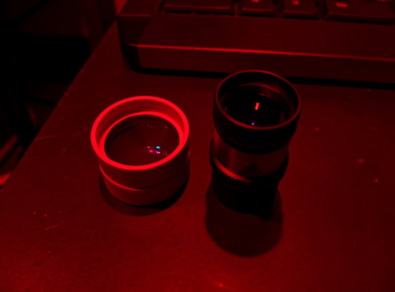 Two nebula filters beside a telescope eyepiece on a dark observing table