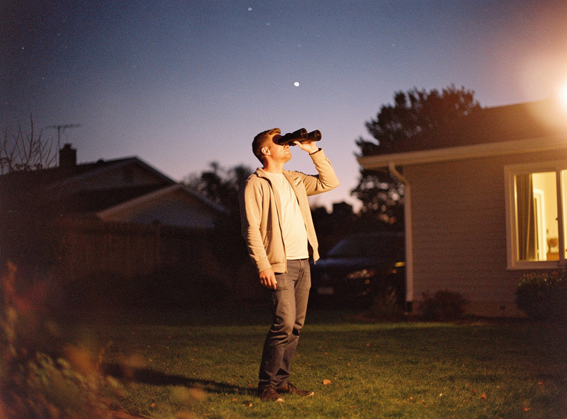 A beginner observing the night sky with handheld binoculars in a suburban backyard