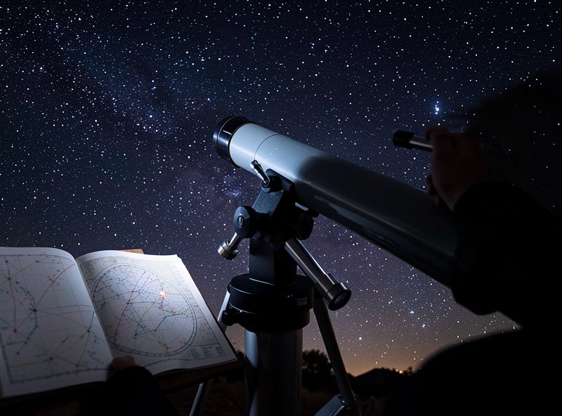 An observer star-hopping by hand at the eyepiece of an equatorial telescope under a starry sky, learning the sky