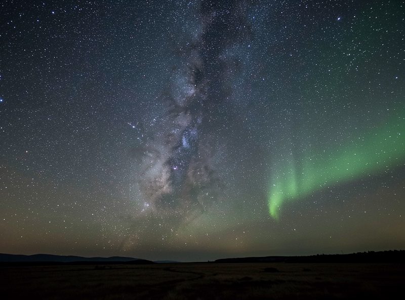 Wide field view of the seasonal night sky arcing over a dark Nordic horizon