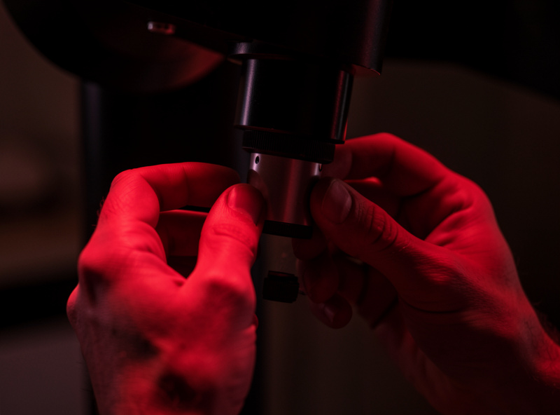 Close-up of an astronomer's hands adjusting a telescope focuser knob under dim red light