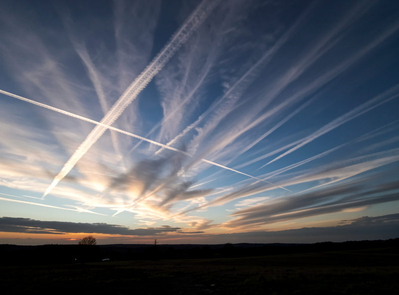 High altitude jet stream clouds streaking across the sky at dusk over a dark landscape